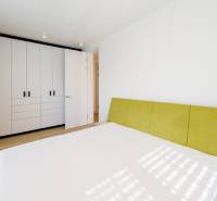 Ein Schlafzimmer mit einem weißen Einbauschrank, einem grünen Kopfteil und einem Boden in Holzoptik.