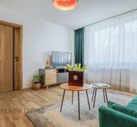 Wohnzimmer in einer 3-Zimmer-Wohnung mit Sofa, Fernseher und Tisch mit Blumen.