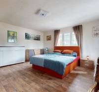 Schlafzimmer im Einfamilienhaus mit Bett, Kommode und Fenster mit Vorhängen.