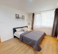 Einfaches Schlafzimmer mit grauem Bett, hellen Accessoires und Holzboden in einer Einzimmerwohnung.