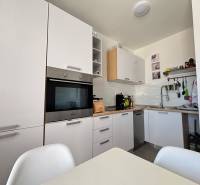 Küche in einer 2-Zimmer-Wohnung mit modernen weißen Schränken und eingebauten Geräten.