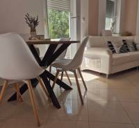Innenraum einer 2-Zimmer-Wohnung mit einem Holztisch, weißen Stühlen und einem bequemen Sofa.