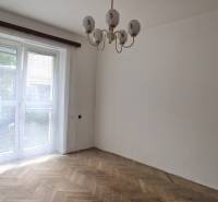 Ein Zimmer in einer 2-Zimmer-Wohnung mit Parkettboden und einem großen Fenster mit weißen Vorhängen.