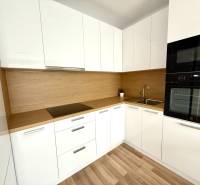 Küche in einer 2-Zimmer-Wohnung mit weißen Schränken und einer Holzarbeitsplatte.