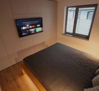 Schlafzimmer im Einfamilienhaus mit Fernseher, großem Bett und Fenster.