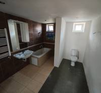 Badezimmer in einem Einfamilienhaus mit Badewanne, Toilette und Waschbecken, braune Fliesen.