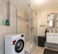 Badezimmer in einer Einzimmerwohnung mit Waschmaschine, Duschkabine und Waschbecken.
