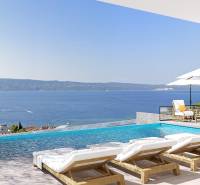 Blick von der Villa in Duće auf das Meer, Terrasse mit Pool, Liegestühlen und Sonnenschirmen.