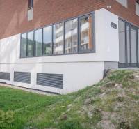 Die Fassade der Geschäftsräume in der Stadt Svit mit großen Fenstern und einem grünen Rasen.