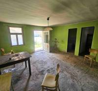 Ein verlassenes Zimmer in einem Einfamilienhaus mit einfacher Einrichtung und offenen Türen nach draußen.