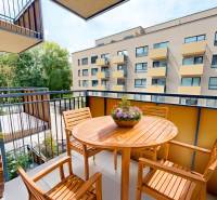 Balkon mit Holzmöbeln in einer 2-Zimmer-Wohnung. Blick auf das Nachbargebäude und Grünflächen.