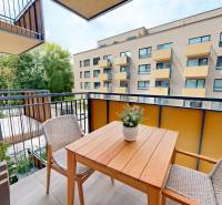 Balkon einer 2-Zimmer-Wohnung mit Holztisch und Stühlen, Blick auf das umliegende Gebäude.