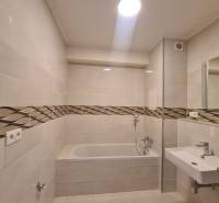 Badezimmer in einer Einzimmerwohnung mit Badewanne und Waschbecken, Keramikfliesen mit Designstreifen.