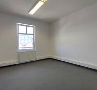 Ein leeres Büro mit einem Fenster, weißen Wänden und grauem Boden, geeignet zur Vermietung.
