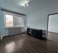 Ein Zimmer in einem Einfamilienhaus mit einem Fenster, dunkler Boden, helle Wände, Möbel an der Wand.