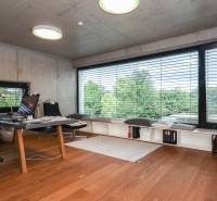 Ein Arbeitszimmer in einem Einfamilienhaus mit großem Fenster und Holzboden, moderne Möbel, Blick auf Bäume.