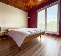 Helles Schlafzimmer in einem Einfamilienhaus mit Holzbalkendecke und großem Fenster.