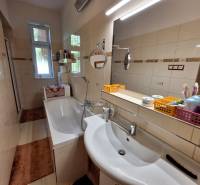 Badezimmer mit Badewanne und Spiegel in einem Einfamilienhaus, ausgestattet mit Regalen und Waschbecken.
