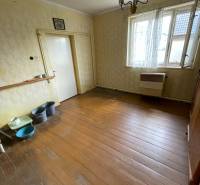 Innenraum eines Einfamilienhauses mit Holzboden, älteren Möbeln und einer hängenden Leuchte.