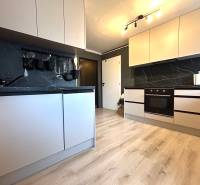 Küche mit weißen Schränken in einer 4-Zimmer-Wohnung, ausgestattet mit einer dunklen Arbeitsplatte.