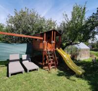 Der Garten des Einfamilienhauses in Topoľčianky mit einem Kinderspielhaus, einer Rutsche und Liegestühlen.