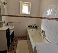 Ein Badezimmer in einem Einfamilienhaus mit eingebauter Badewanne und Waschbecken, gefliest mit hellen Fliesen.