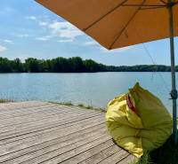Ein Holzsteg und ein Sitzsack unter einem Sonnenschirm am See in Vojka nad Dunajom.