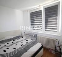 Schlafzimmer in einer 2-Zimmer-Wohnung mit Bett, Kinderbett und großem Fenster.