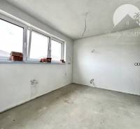 Ein leerer Raum in einem Einfamilienhaus mit großen Fenstern und unfertigem Boden.