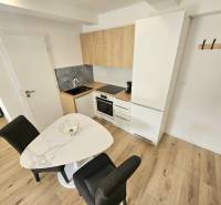 Küche in einer Einzimmerwohnung mit Holzboden, Esstisch und weißen Schränken.