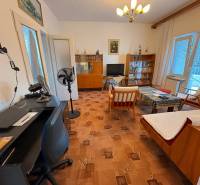 Wohnzimmer in einem Einfamilienhaus mit älteren Möbeln und einem Tischventilator.