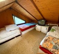Dachzimmer in einer Hütte mit drei Betten und einem Fernseher.