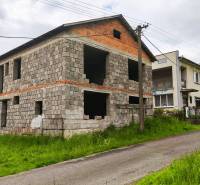 Unvollendetes Einfamilienhaus in Čelovce, umgeben von Grün, an einer schmalen Straße gelegen.