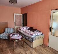 Ein Zimmer in einer Einzimmerwohnung mit einem Bett, einem Sessel und einem Tisch auf einem Parkettboden.