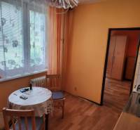 Küche in einer Einzimmerwohnung mit Tisch, Stühlen und Vorhängen am Fenster.
