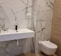 Badezimmer mit hängendem WC, Keramikwaschbecken und Marmorfliesen in einer 4-Zimmer-Wohnung.