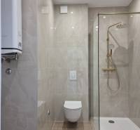 Badezimmer in einer 4-Zimmer-Wohnung mit Toilette, Dusche und glatten Fliesen.