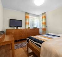 Schlafzimmer im Einfamilienhaus mit Holzmöbeln, Fernseher und bunten Vorhängen.