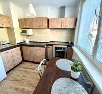Küche in einer 2-Zimmer-Wohnung mit hellem Holz, weißen Geräten und einem Tisch.