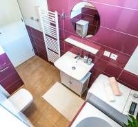 Badezimmer in einer 2-Zimmer-Wohnung mit Waschmaschine, Waschbecken, rundem Spiegel und rosa Fliesen.