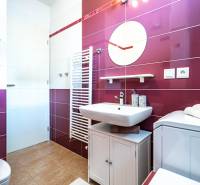 Badezimmer in einer 2-Zimmer-Wohnung mit weiß-rosa Fliesen, Waschbecken und Waschmaschine.