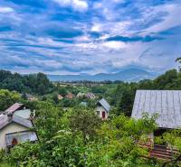 Blick auf die Hütten in Mojš, umgeben von üppigem Grün und Hügeln unter dramatischem Himmel.