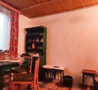 Das Innere einer Hütte mit Holzbalkendecke, Tisch, Stühlen und Regal.