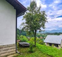 Der Blick von der Hütte in Mojš zeigt Dächer, Grünflächen und entfernte Hügel unter einem bewölkten Himmel.