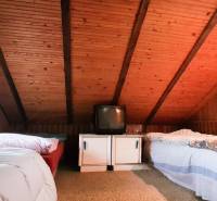 Dachboden-Schlafzimmer in einer Hütte mit Holzverkleidung, Betten und einem älteren Fernseher.