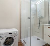 Badezimmer in einer 2-Zimmer-Wohnung mit Waschmaschine, Duschkabine und weißen Fliesen.