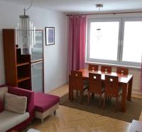 Essbereich mit Holztisch in einer 3-Zimmer-Wohnung, ergänzt durch rosa Vorhänge und ein Sofa.