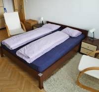 Schlafzimmer in einer 3-Zimmer-Wohnung mit einem Holzbett, einem Stuhl und einem weißen Teppich.