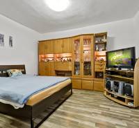 Schlafzimmer mit Doppelbett, Wohnwand aus Holz und Fernseher in einer Zweizimmerwohnung.