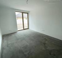 Ein leerer Raum mit einem großen Fenster in einem Einfamilienhaus, mit unfertigem Boden.